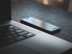 Karanlık bir masanın üzerinde, açık bir dizüstü bilgisayarın yanında duran bir akıllı telefon