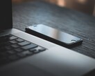 Karanlık bir masanın üzerinde, açık bir dizüstü bilgisayarın yanında duran bir akıllı telefon