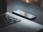 Karanlık bir masanın üzerinde, açık bir dizüstü bilgisayarın yanında duran bir akıllı telefon