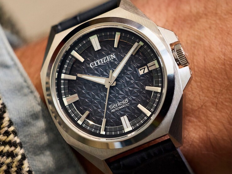 Citizen Series 8 831 otomatik saat, yanık turuncu ve kahverengi geometrik kadranı, altın rengi kasası ve çerçeve ile entegre altın rengi H-link bileziğiyle bir kişinin bileğinde.