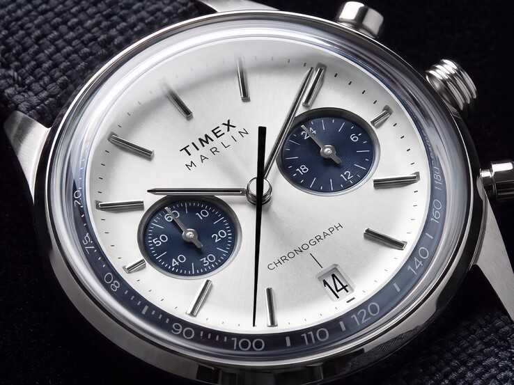 Timex Marlin Jet Chronograph TW2Y89900 modelinin gümüş-beyaz kadranı, lacivert alt kadranları, yapıştırmalı saat işaretleri, çubuk ibreleri, takimetre ölçeği ve tarih penceresini gösteren yakın çekim fotoğrafı.