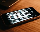 Ahşap bir masanın üzerinde duran bir akıllı telefon; ekranında bir dizi fotoğraf görünüyor