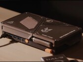 Masa üzerinde duran, mini bir bilgisayar, açıkta bulunan soğutma delikleri, USB bağlantı noktaları ve turuncu renkli güç düğmelerine sahip, özel olarak tasarlanmış kompakt bir oyun konsolu.