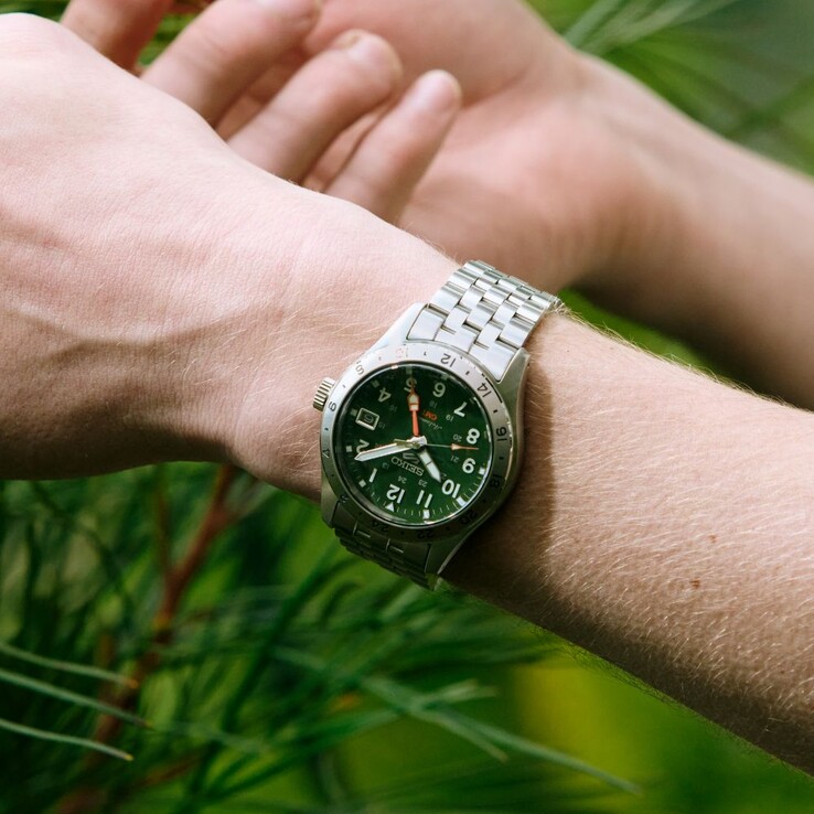 Yeşil kadranı, sabit paslanmaz çelik 24 saatlik çerçeve, turuncu GMT ibresi ve beş halkalı çelik bileziği ile öne çıkan Seiko 5 Sports Field GMT HDB001 modelinin önden görünümü.