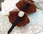 Deniz haritaları ve hasır örgü üzerinde fotoğraflanmış, beyaz Romen rakamlı kadranı ve siyah deri kayışı olan altın tonlu Noah × Timex Boatswain saat.