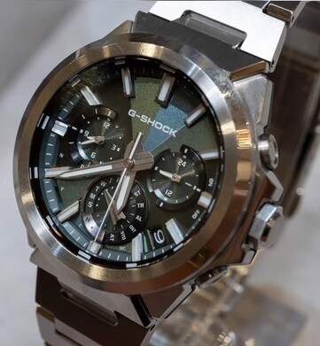 Yeşil kadranlı Casio G-Shock GST-W1000D-3A modelinin yakın çekim görüntüsü; geometrik dokulu kadranı, üç alt kadranı, ışıklı işaretleri ve parlak paslanmaz çelik çerçevesini göstermektedir.