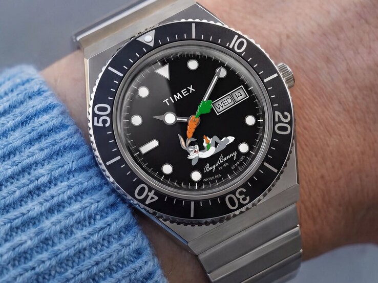 Bilekte takılı Timex Looney Tunes x M79 Automatic saatinin Bugs Bunny figürlü siyah kadranında havuç şeklinde bir saniye ibresi ve gün-tarih göstergesi bulunuyor; saat ayrıca siyah döner bir bezele sahip.