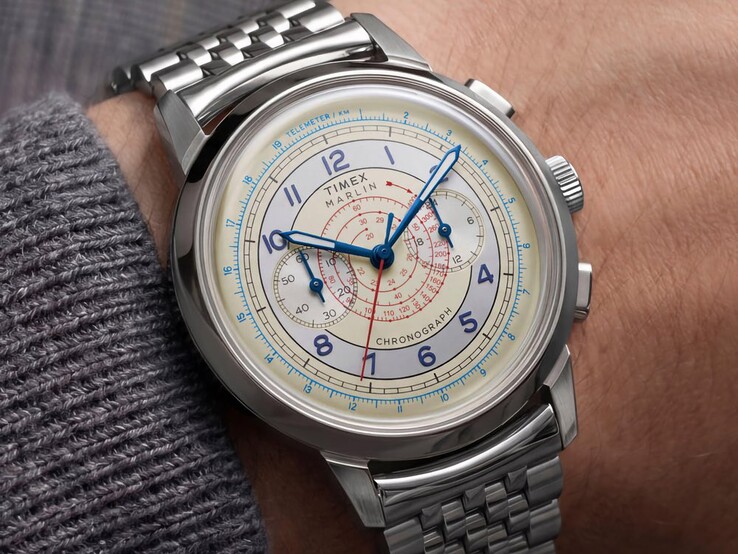 Krem rengi kadranı, mavi ibreleri ve paslanmaz çelik bileziği olan Timex Marlin Neo Classic Kronograf, bir kişinin bileğinde takılıdır.