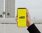 Sarı bir ekranda "eSIM" kelimesinin büyük harflerle yazıldığı bir akıllı telefonu tutan bir el.