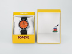 Turuncu kadranlı Seiko 5 Sports x Popeye HDB013 otomatik saat, sınırlı sayıda üretilmiş sarı sunum kutusunun yanında duruyor.