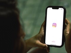 İki eliyle bir akıllı telefon tutan kadın; ekranda Instagram başlangıç ekranı görünüyor