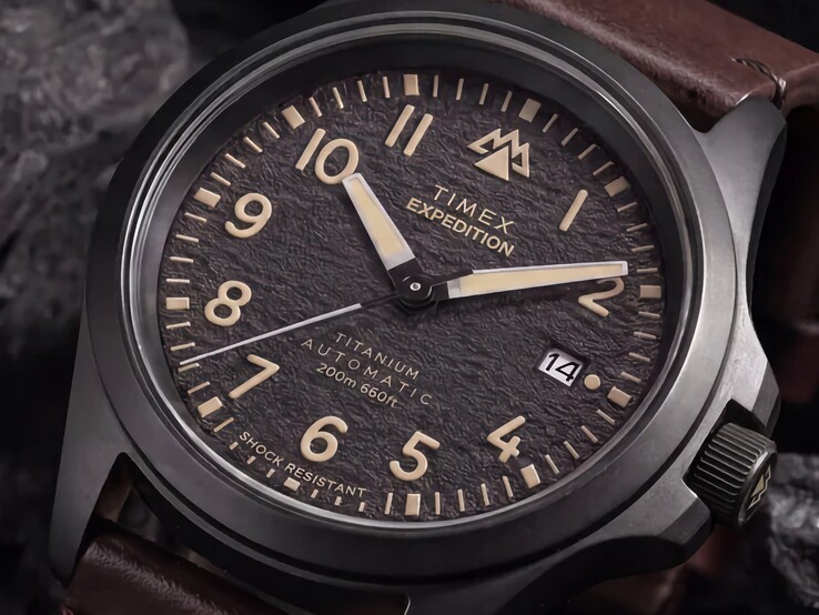 Timex Expedition Field Post Titanium saatinin, Arap rakamları, ışıklı ibreler ve işaretçiler ile tarih penceresine sahip dokulu siyah kadranının yakın çekimi.