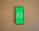 Ahşap bir masanın üzerinde, logosu ile birlikte WhatsApp'ın yeşil başlangıç ekranını gösteren bir akıllı telefon.