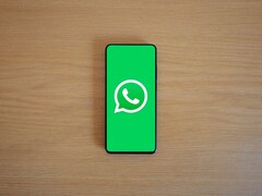Ahşap bir masanın üzerinde, logosu ile birlikte WhatsApp'ın yeşil başlangıç ekranını gösteren bir akıllı telefon.