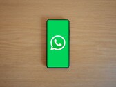 Ahşap bir masanın üzerinde, logosu ile birlikte WhatsApp'ın yeşil başlangıç ekranını gösteren bir akıllı telefon.